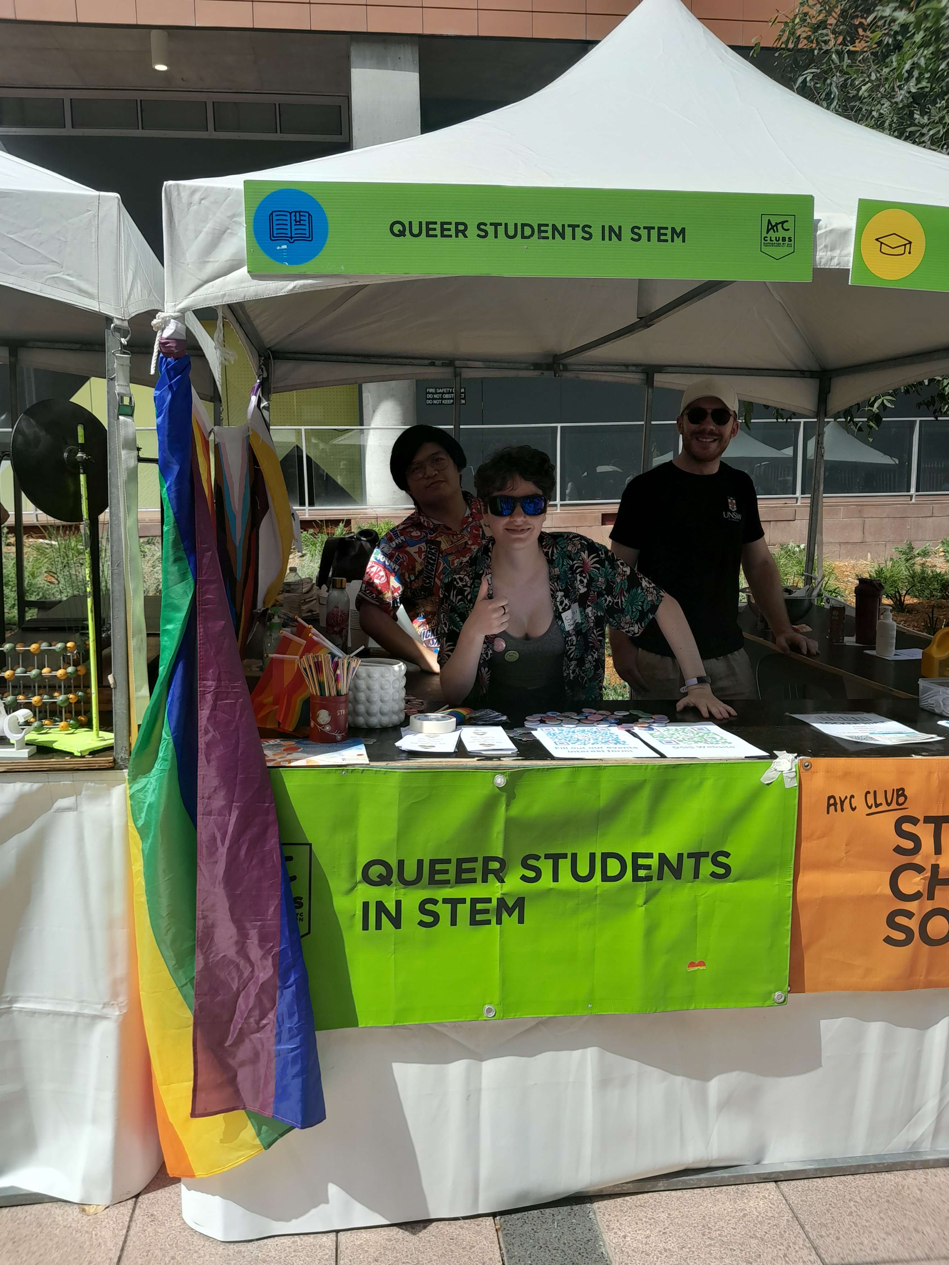 Two people standing in a stall with a banner that reads Queer Students in STEM